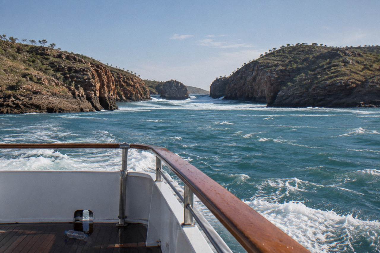A cruise boat crossing open water between rocky islands in the Kimberley
